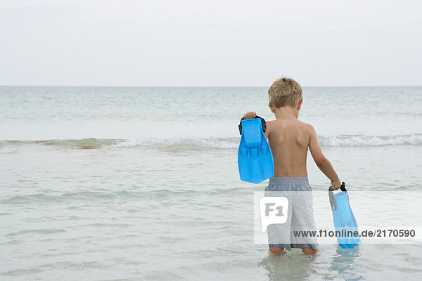 Junge steht knietief im Wasser  trägt Flossen  Rückansicht