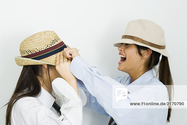 Teenagermädchen zieht Hut über das Gesicht ihres Freundes  lacht