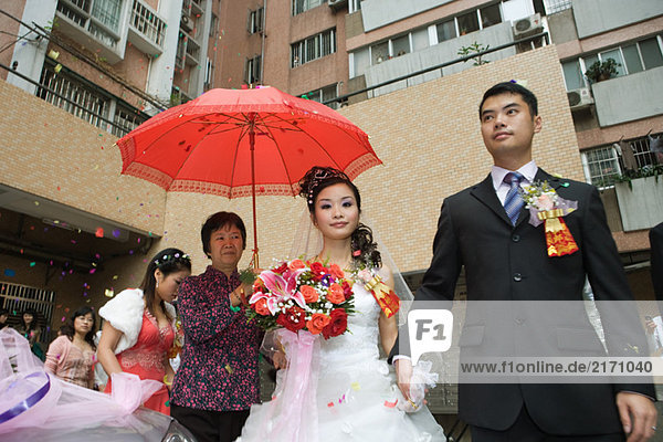Chinesische Hochzeit  Braut und Bräutigam verlassen unter Konfetti  Braut mit rotem Sonnenschirm bedeckt