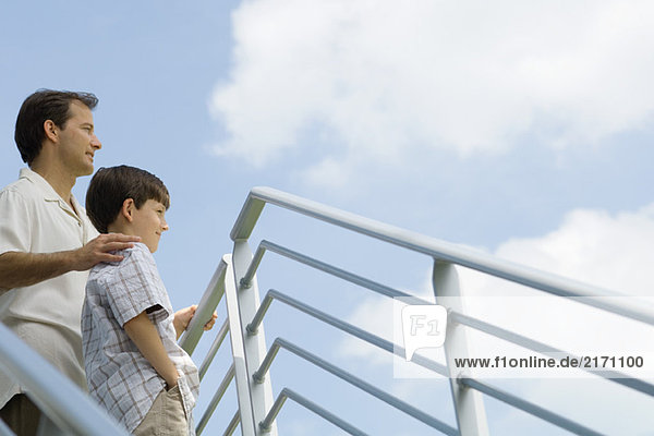 Father and son standing by railing looking at sky  low angle view