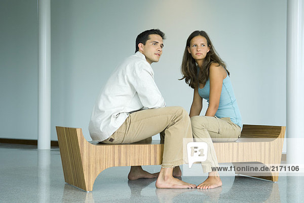 Young couple sitting face to face on bench  both looking away