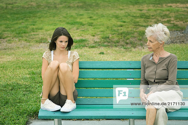 Teenagermädchen sitzt neben Großmutter auf Bank  beide Stirnrunzeln