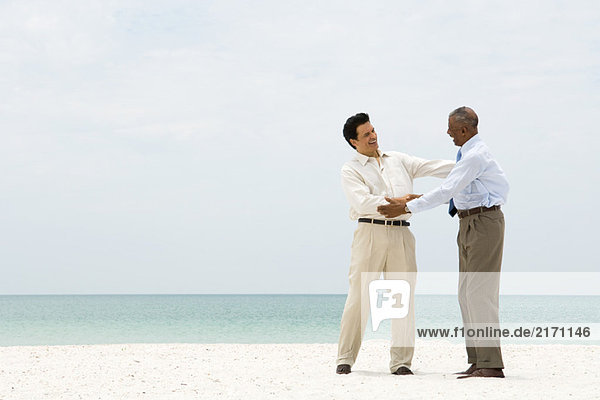 Zwei Geschäftsleute schütteln sich am Strand die Hand und lächeln sich an.