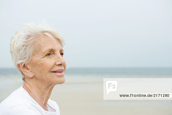 Seniorin lächelt  schaut weg  Strand im Hintergrund