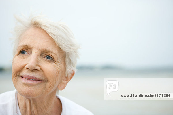 Senior woman smiling  looking up  beach in background