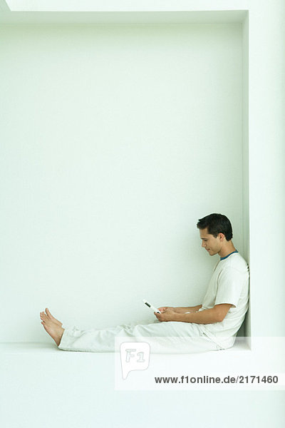 Man sitting on ledge using cell phone  full length  side view