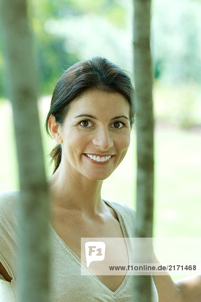 Woman smiling at camera through trees  portrait