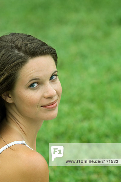 Teen girl looking over shoulder at camera  cropped  head and shoulders  grass in background