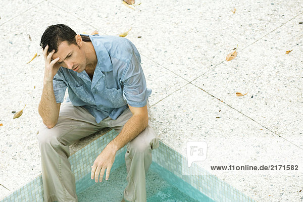 Mann sitzend mit Füßen im Pool  Kopf haltend  hohe Winkelansicht