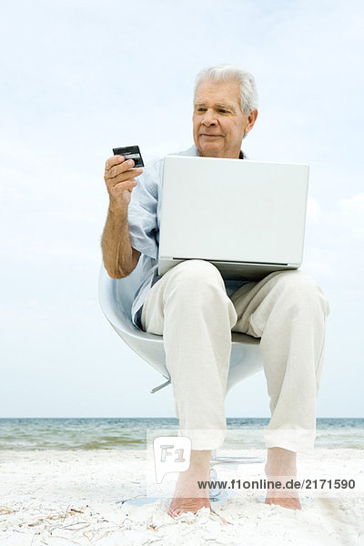 Senior Mann mit Laptop am Strand  die Online-Einkauf mit Kreditkarte