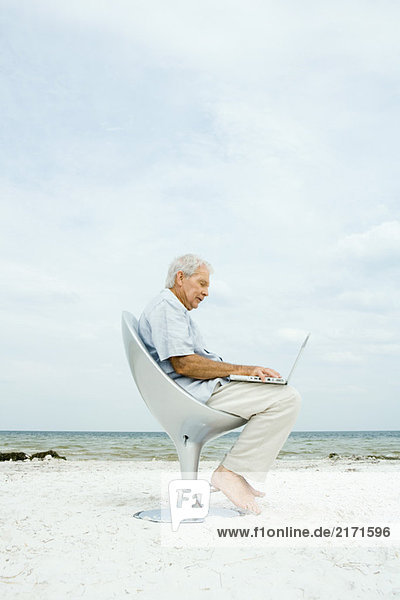 Senior man using laptop on beach  side view