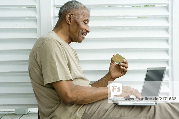 Senior Mann mit Laptop  die Online-Einkauf mit Kreditkarte