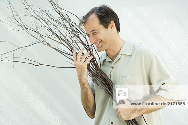 Mann hält den Arm voller Zweige  lächelnd  wegschauend