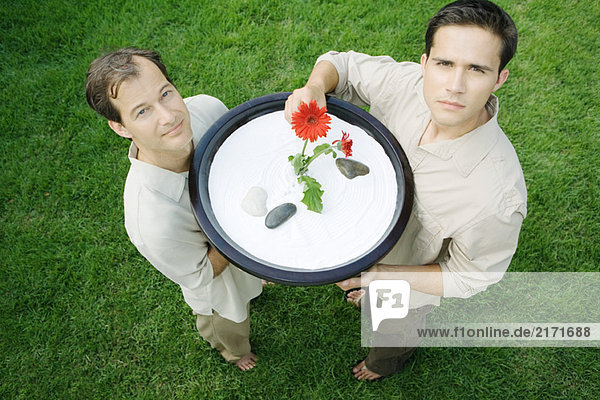 Two men holding up rock garden  one touching flower  high angle view