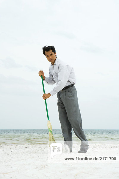 Mann am Strand stehend  mit Besen fegend  mit Blick auf die Kamera