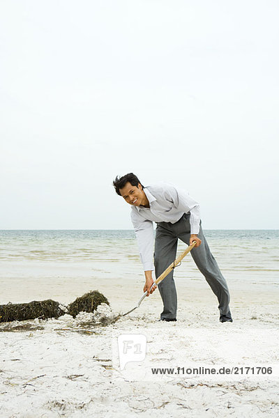 Mann am Strand schaufelt Sand mit Schaufel  lächelt in die Kamera  volle Länge