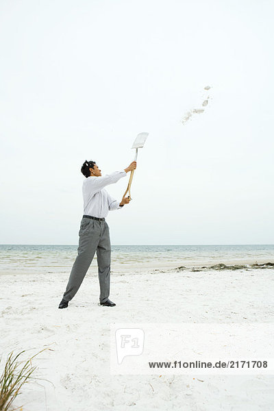 Mann am Strand  der Schaufel hochhält  Sand wirft  volle Länge