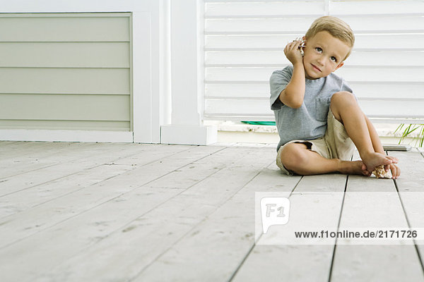Boy sitting on the ground listening to seashell  smiling