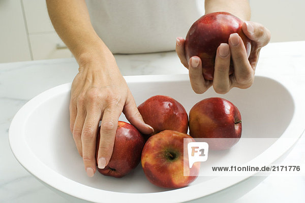 Frau legt Äpfel in Obstschale  abgeschnittene Handansicht