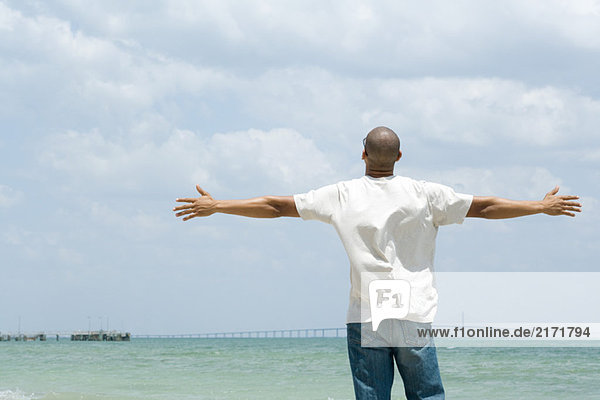 Man standing by the sea with arms outstretched  rear view