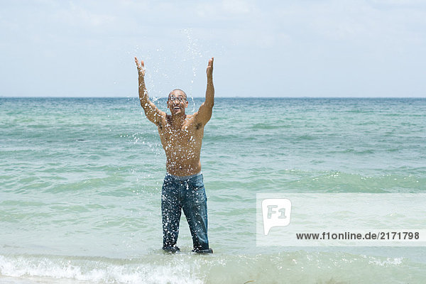 Man splashing in ocean  arms raised