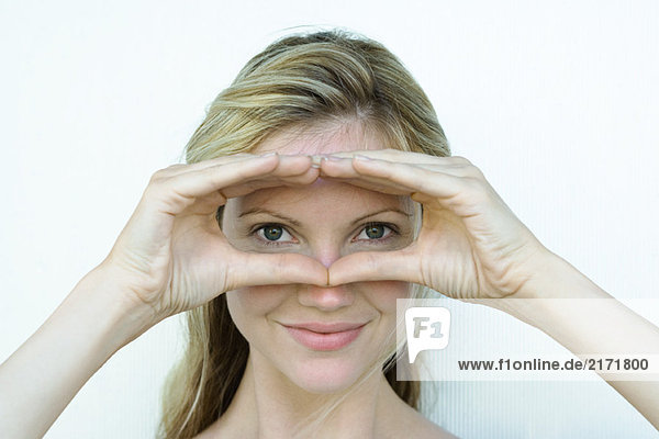 Woman looking through finger frame at camera  smiling