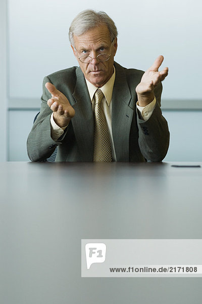 Businessman seated  gesturing with hands  looking at camera