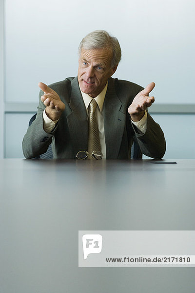 Businessman seated  gesturing with hands  looking away