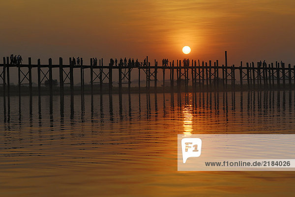 Silhouette of group of people walking on bridge across river at dusk  U Bein Bridge  Amarapura  Myanmar