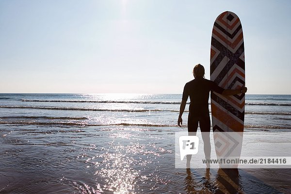 Mann am Strand stehend mit Surfbrett.