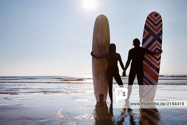 Paar am Strand stehend mit Surfbrettern an den Händen.