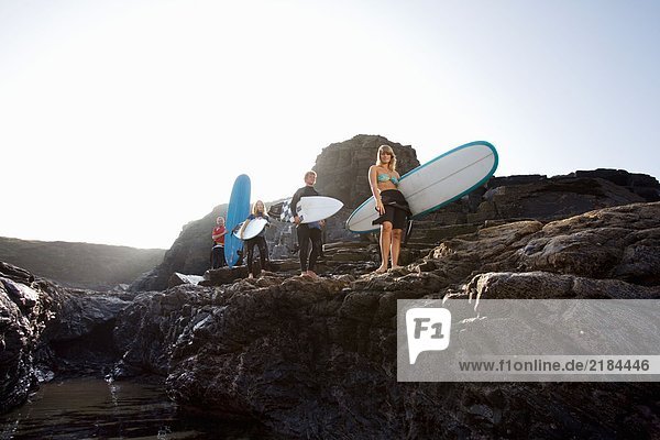 Vier Leute mit Surfbrettern auf großen Felsen lächelnd.