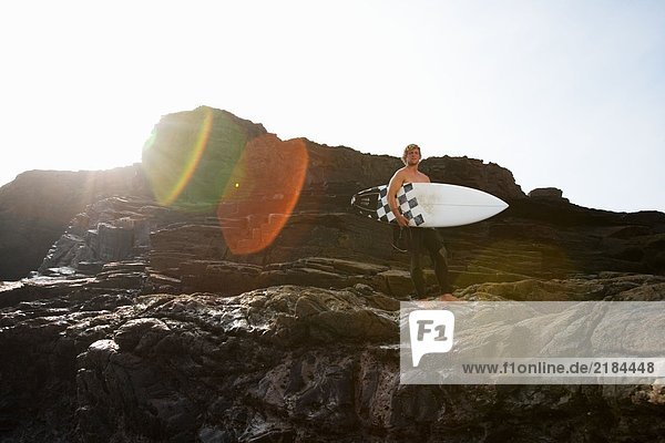 Mann hält Surfbrett auf großen Felsen.