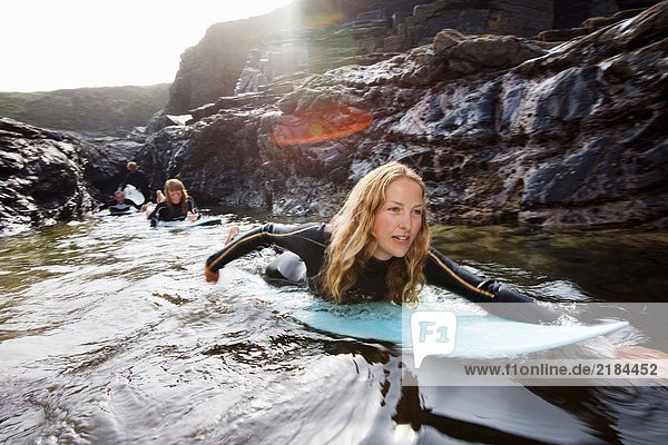 Vier Leute liegen auf Surfbrettern im Wasser und lächeln.