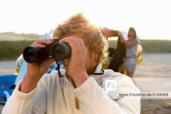Man on beach with binoculars with woman unloading van at the beach .
