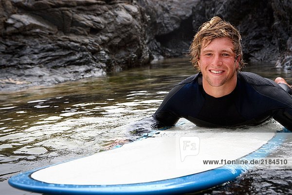 Mann auf dem Surfbrett im Wasser liegend lächelnd.