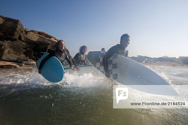 Vier Leute laufen mit lächelnden Surfbrettern ins Wasser.