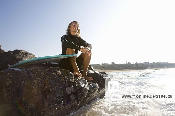 Frau sitzt auf großen Felsen mit lächelndem Surfbrett.