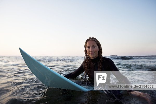 Frau sitzt auf dem Surfbrett im Wasser.