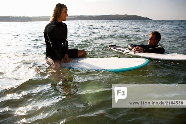Ein Paar schwebt auf Surfbrettern im Wasser und lächelt.