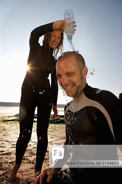 Frau gießt Wasser über den Kopf des lachenden Mannes.