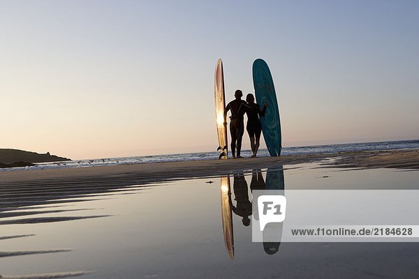 Paar am Strand stehend mit Surfbrettern.