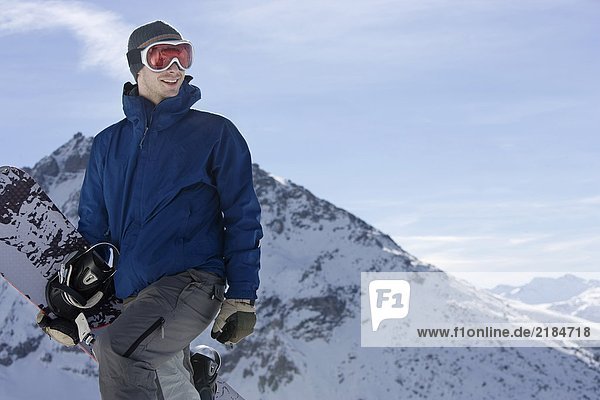 Male snowboarder standing on top of mountain ridge with snowboard