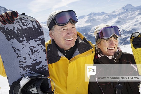 Mature couple in ski-wear holding Skis and snowboard on mountain  close-up  portrait