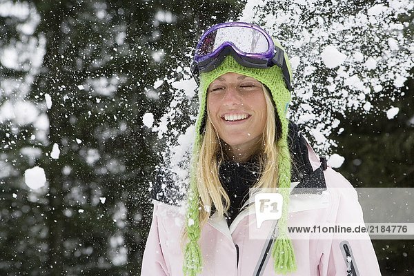 Snowball exploding on young blonde woman wearing ski-wear in forest