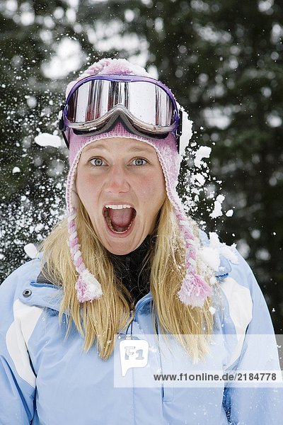 Schneeball explodiert auf einer jungen blonden Frau  die im Wald Skibekleidung trägt.