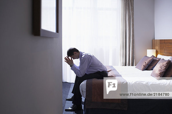 Man sitting on edge of bed with head in hands