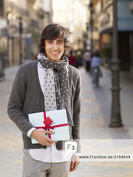 Young man standing in street holding gift  smiling  portrait