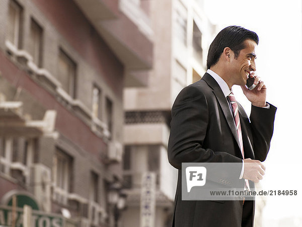 Young businessman standing in street using mobile phone  smiling