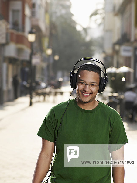 Young man standing in street wearing headphones  smiling  portrait